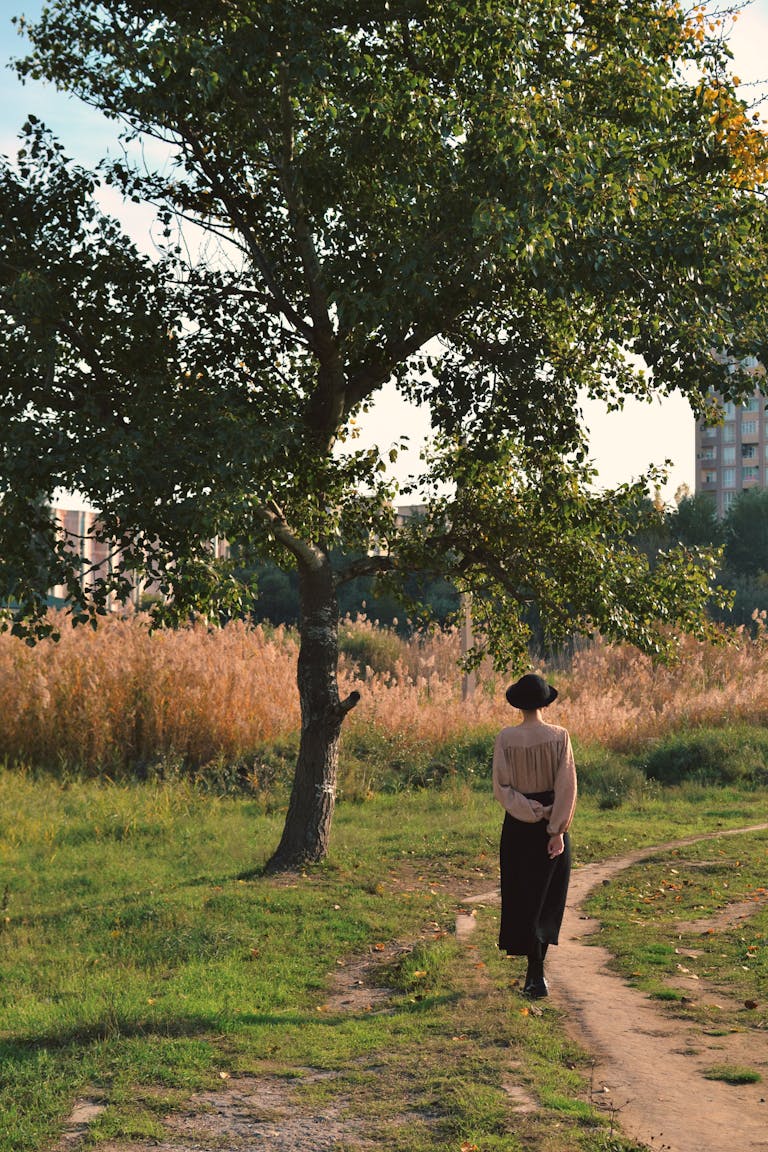 A woman strolls along a park path during autumn, surrounded by trees and nature.